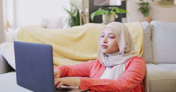在家戴头巾的混血女人坐在地板上用笔记本电脑工作的视频