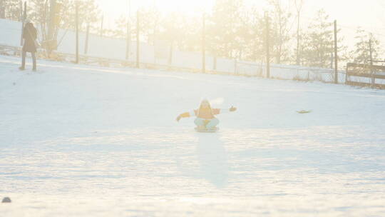 小女孩坐在雪盘上开心的滑雪