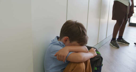 悲伤的高加索男孩坐在学校走廊上，用手捂住头的视频