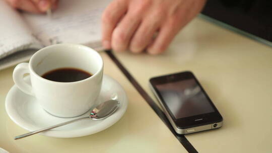 男子在放有咖啡和手机的桌子上写字视频素材模板下载