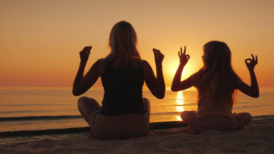 妈妈和女儿在日落时在海边冥想
