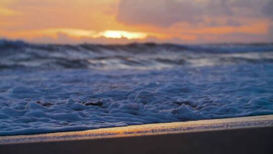 日落时在海滩岸边手持近拍海浪