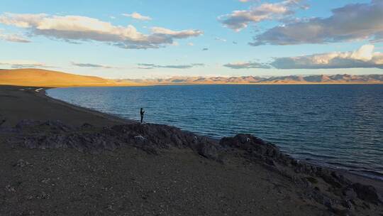 航拍黄昏时分一个人站在纳木错湖边的石头上