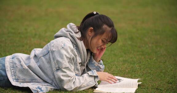 大学校园里女学生趴在草地上看书学习休闲