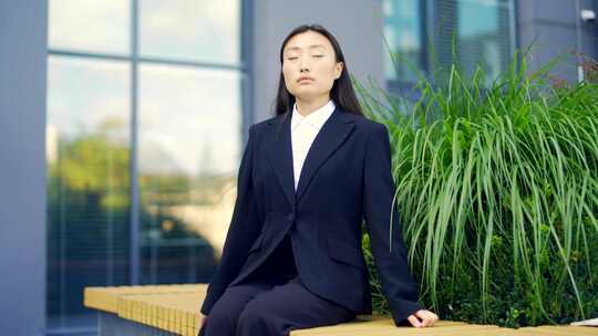 亚洲女上班族放松，冥想户外坐在城市背景城