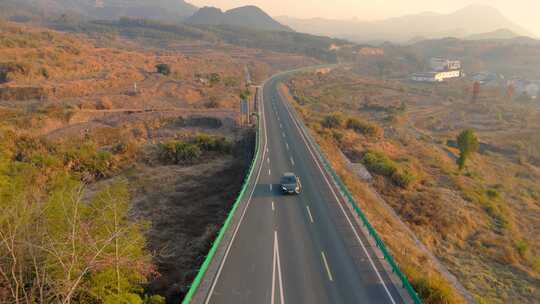 迎着朝霞在空旷山路上行驶的汽车