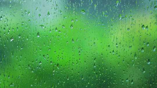雨水落在窗户玻璃上窗外绿色背景的治愈氛围