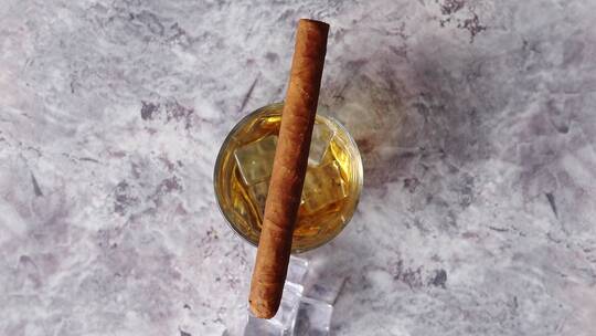 一杯加冰块的威士忌和一根雪茄在桌上