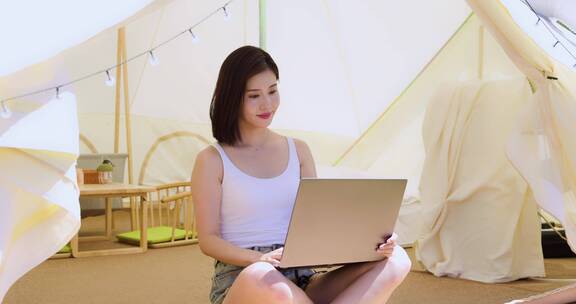 一个美女坐帐篷里使用电脑享受阳光