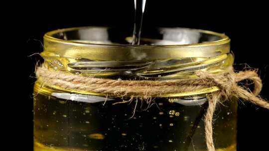 蜂蜜从勺子纺锤上流下来，进入一个黑色背景上有蜂蜜的罐子。