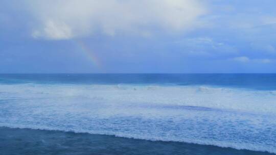 蓝天白云彩虹下波涛汹涌的海面