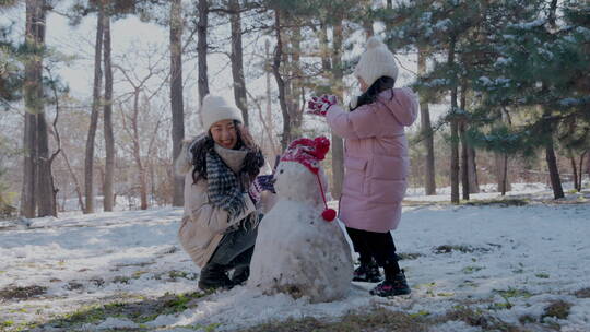 年轻妈妈和女儿在雪地里堆雪人