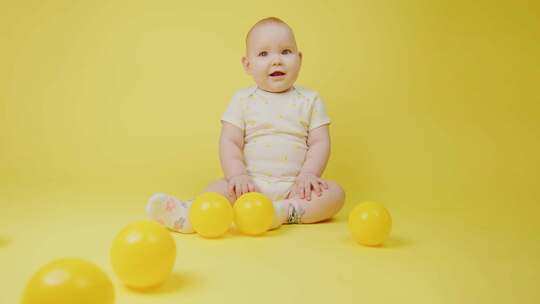 黄色背景上有黄色球的快乐女婴快乐的婴儿微