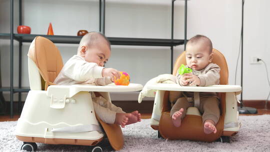 双胞胎宝宝坐在玩具椅子里玩玩具