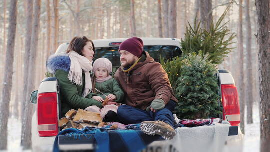 在雪地的汽车上抱着孩子过圣诞节的父母