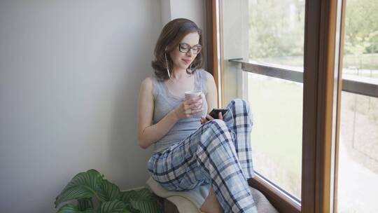 女人坐在窗户旁听音乐喝茶视频素材模板下载