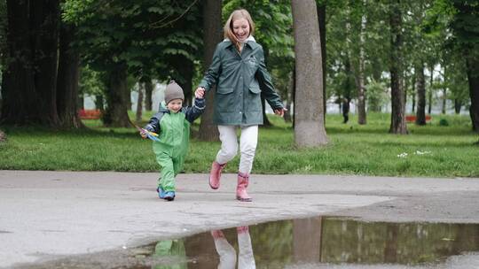 母亲带着穿着雨靴的孩子在公园水坑玩耍