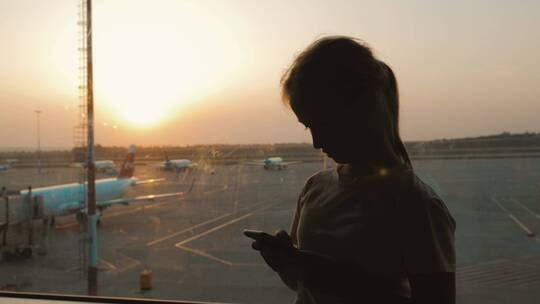 黄昏女人在机场玩手机剪影