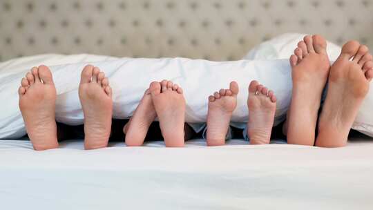 舒适家庭卧室床上毯子下的家庭脚