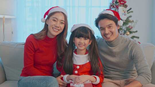 亚洲幸福家庭的肖像戴着圣诞老人帽，坐在客厅里。