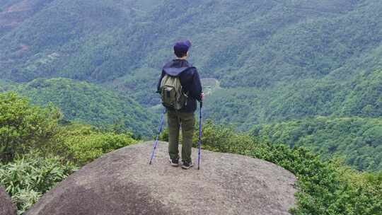 背包客山顶持杖眺望山林