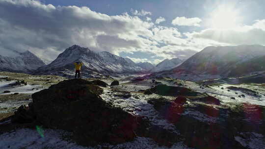 孤独的登山者在雪山上休息，高高的云层映入阳光下，登山者伸手