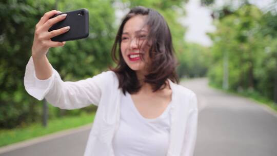城市女青年在公园路上用手机和朋友视频聊天