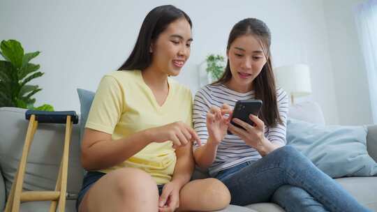 亚洲女性截肢者与漂亮的朋友在家里使用手机。