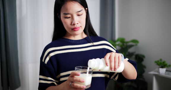 一个年轻女人把牛奶倒进餐桌上的玻璃杯里。