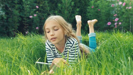 女孩在绿色的草地上快乐的用耳机听着音乐