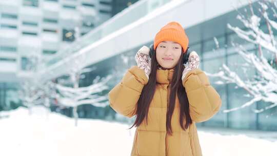 年轻美丽的亚洲女人在冬天下雪天听耳机里的