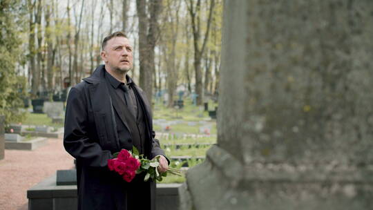 男人手捧鲜花站在墓碑前