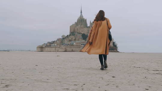 后视镜放大在史诗圣米歇尔山的海沙上缓慢行走的时尚旅游女性