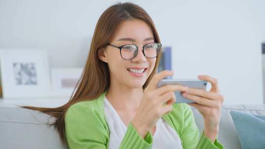 亚洲电子竞技游戏玩家女人在家里的客厅里用手机玩手机游戏时感到快乐。