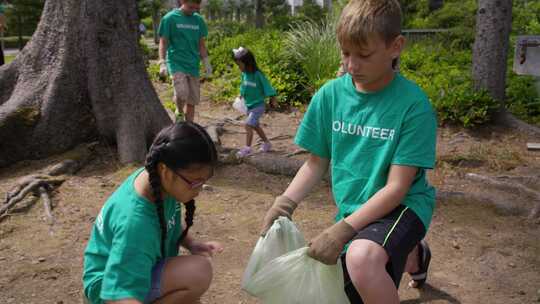 志愿者儿童在公园户外将垃圾放入回收袋