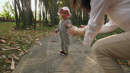 妈妈鼓励可爱的小婴儿在户外公园学走路