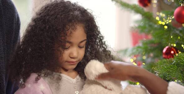 女孩坐在圣诞树下玩毛绒玩具熊