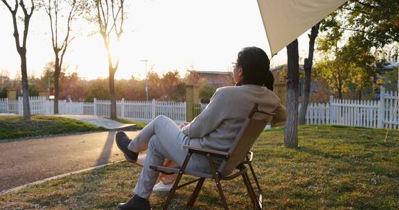 中老年夫妻搂着肩膀坐在露营地天幕下看夕阳