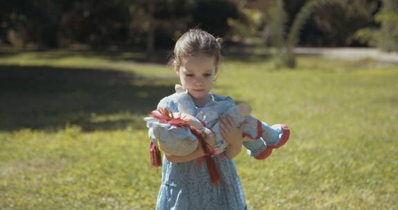 女孩抱布偶站在草地上