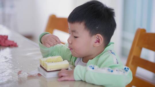 小男孩坐在家里的餐桌上吃美味的巧克力蛋糕
