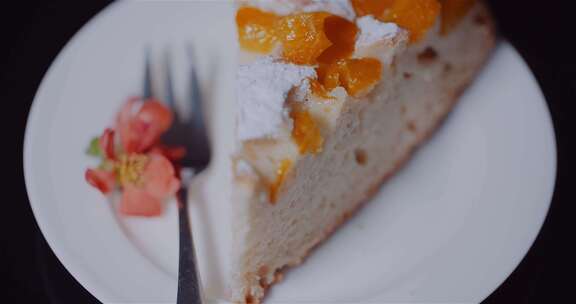 盘子上叉子旁边的一片用糖粉装饰的水果蛋糕