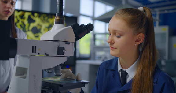 迷人的高加索学生女孩在课堂上通过显微镜观