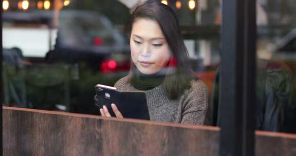 女人在城市咖啡馆喝茶，看着智能手机