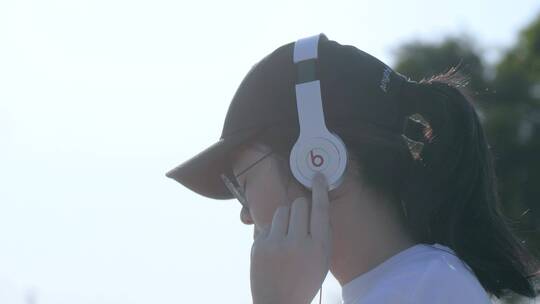 戴着鸭舌帽的女孩在海边用有线耳机听歌视频素材模板下载