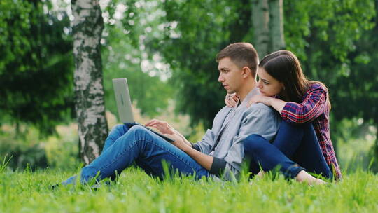 情侣坐在草坪上玩电脑