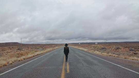 穿着黑色衣服的女人独自走在荒野的笔直道路