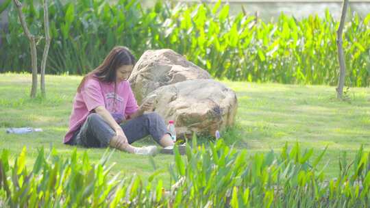女游客公园休闲坐在草地上看手机