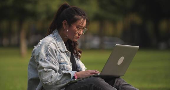 一位女大学生坐在校园草地上用笔记本电脑