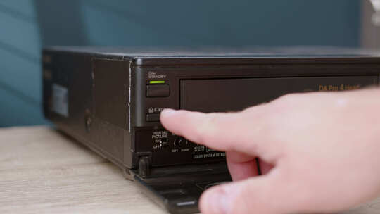 男人按下按钮从VHS播放器中取出带有标签机密磁带的旧黑色磁带