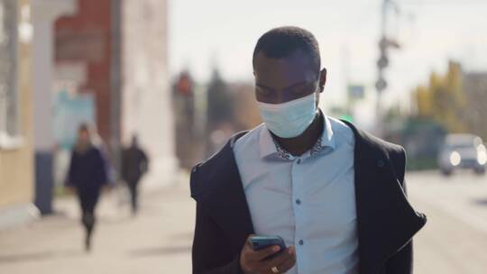 非洲人戴着口罩走在城市里玩手机视频素材模板下载